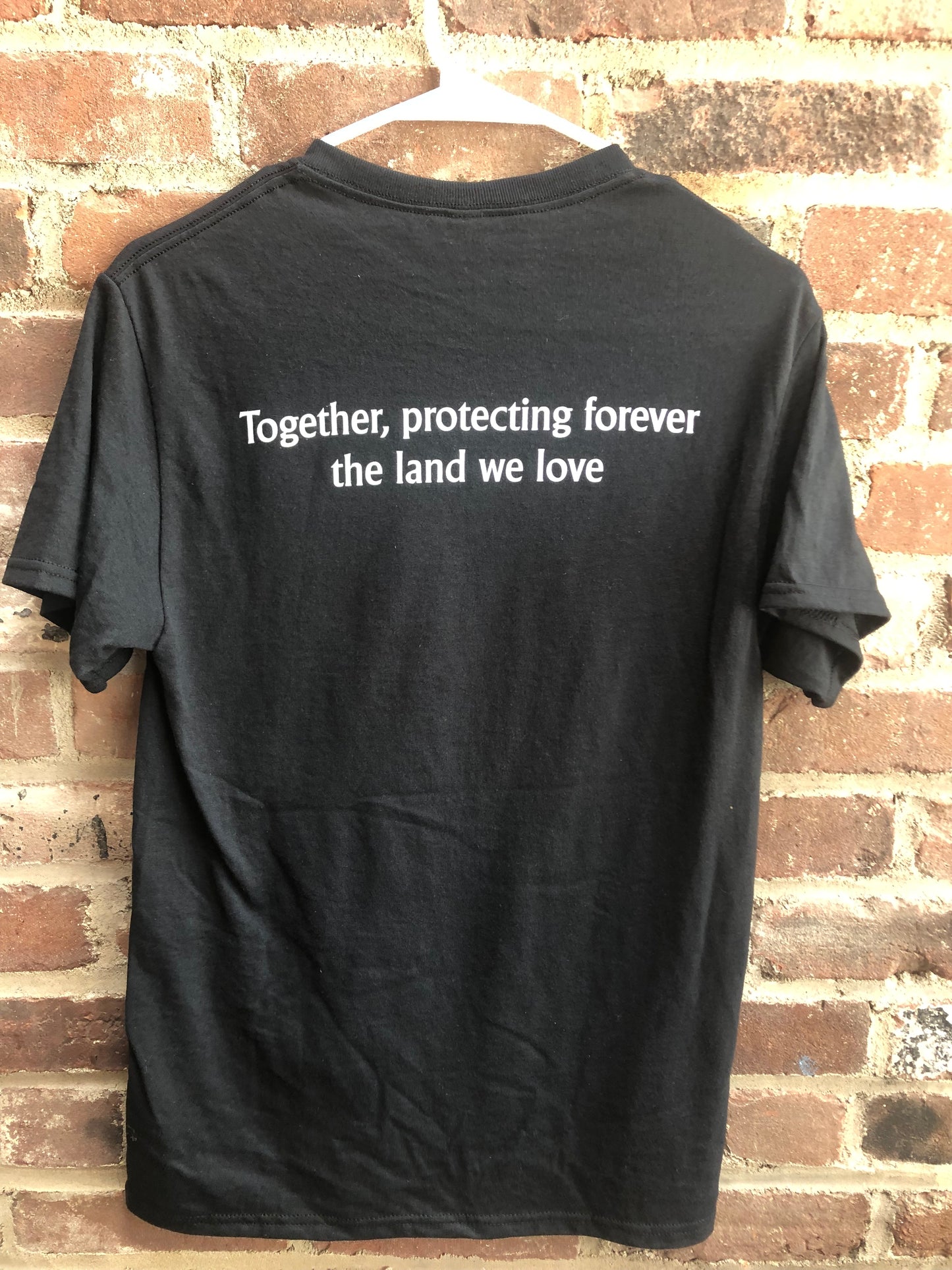 The back of the black t-shirt, that has a message on the back reading "Together, protecting the land that we love." 