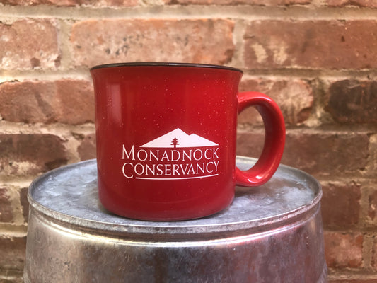 A red coffee mug with the Monadnock Conservancy logo in white