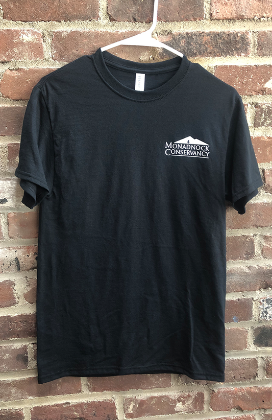 a black t-shirt with the Monadnock Conservancy logo over heart, in white.
