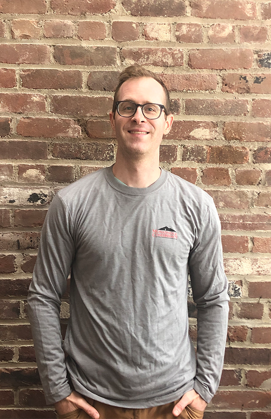 Alex Metzger models the gray, long sleeve shirt with the Monadnock Conservancy's logo in red. 